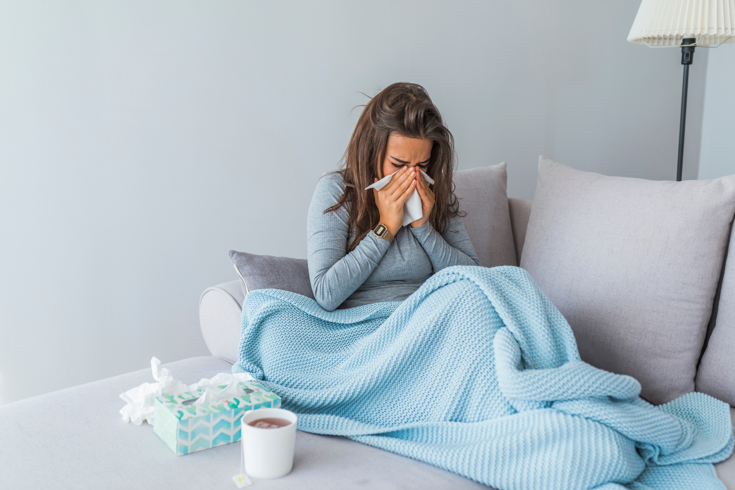 lady sick on the couch, blowing her nose